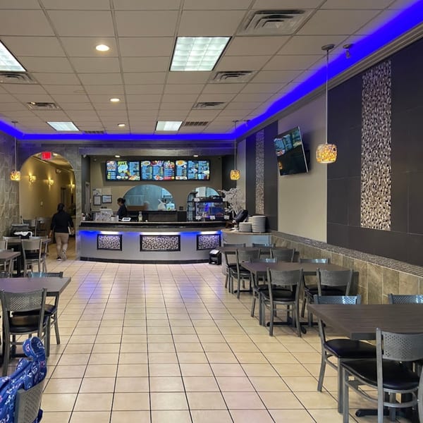 Interior of Tempura Halal Indo-Pak Grill with dining tables, a service counter, and blue accent lighting.