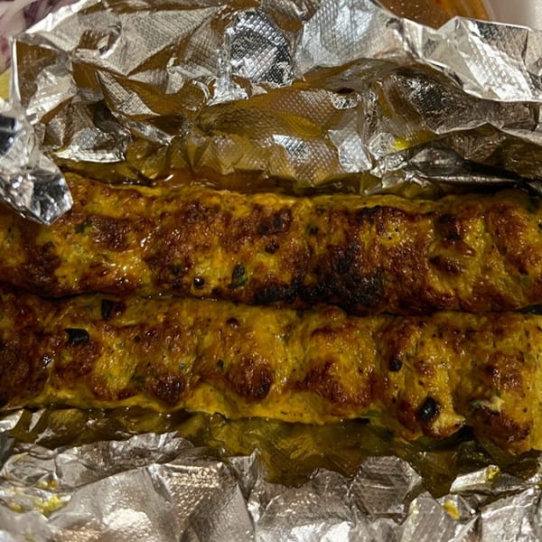 Two golden-brown seekh kebabs, charred in spots, resting in crinkled aluminum foil.
