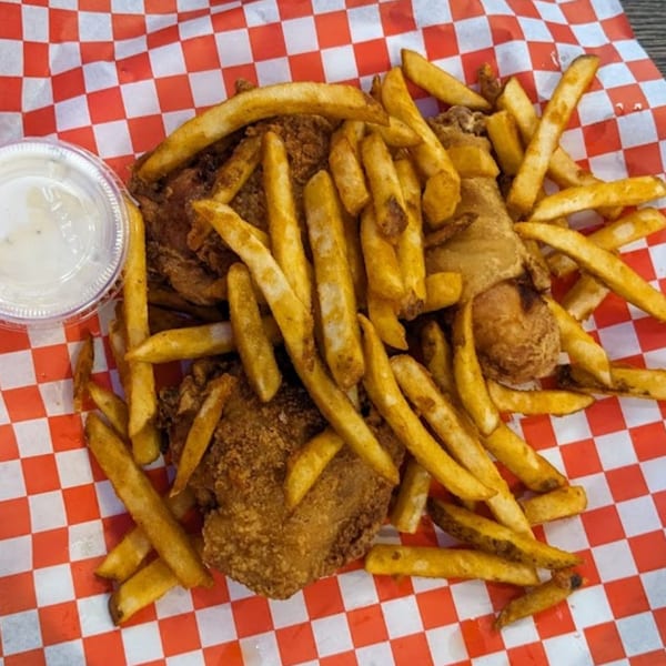 Crispy fried chicken and golden french fries served with a side of sauce on red and white checkered paper.