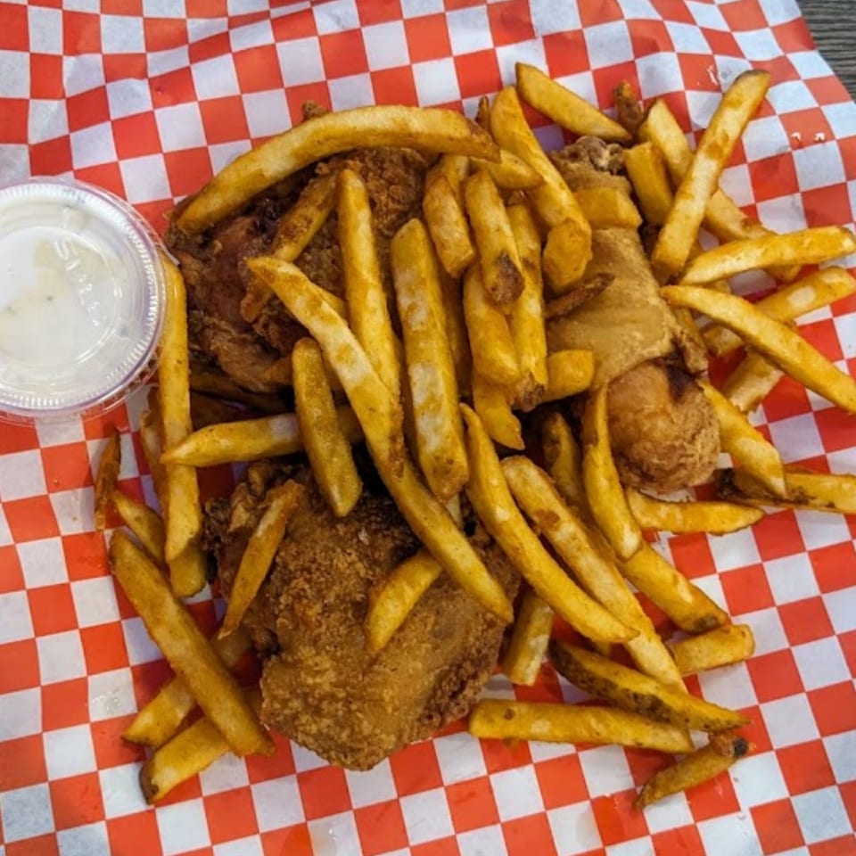 Crispy fried chicken and golden french fries served with a side of sauce on red and white checkered paper.