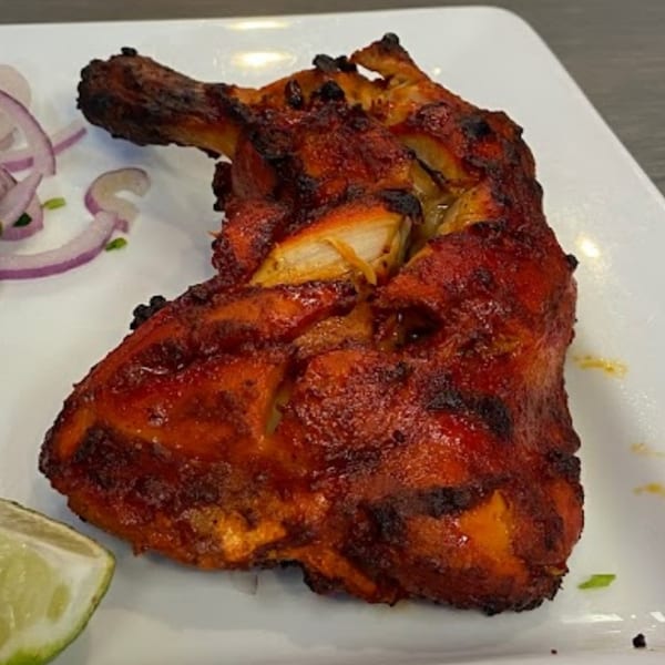 Pakistani-style grilled chicken leg quarter, garnished with red onion slices and a lime wedge.