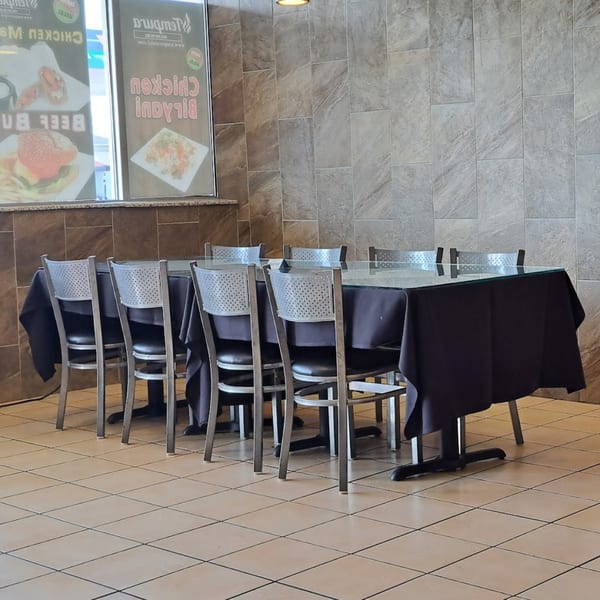 Empty dining area with black-draped tables, metal chairs, and menu posters for Tempura Halal Indo-Pak Grill.