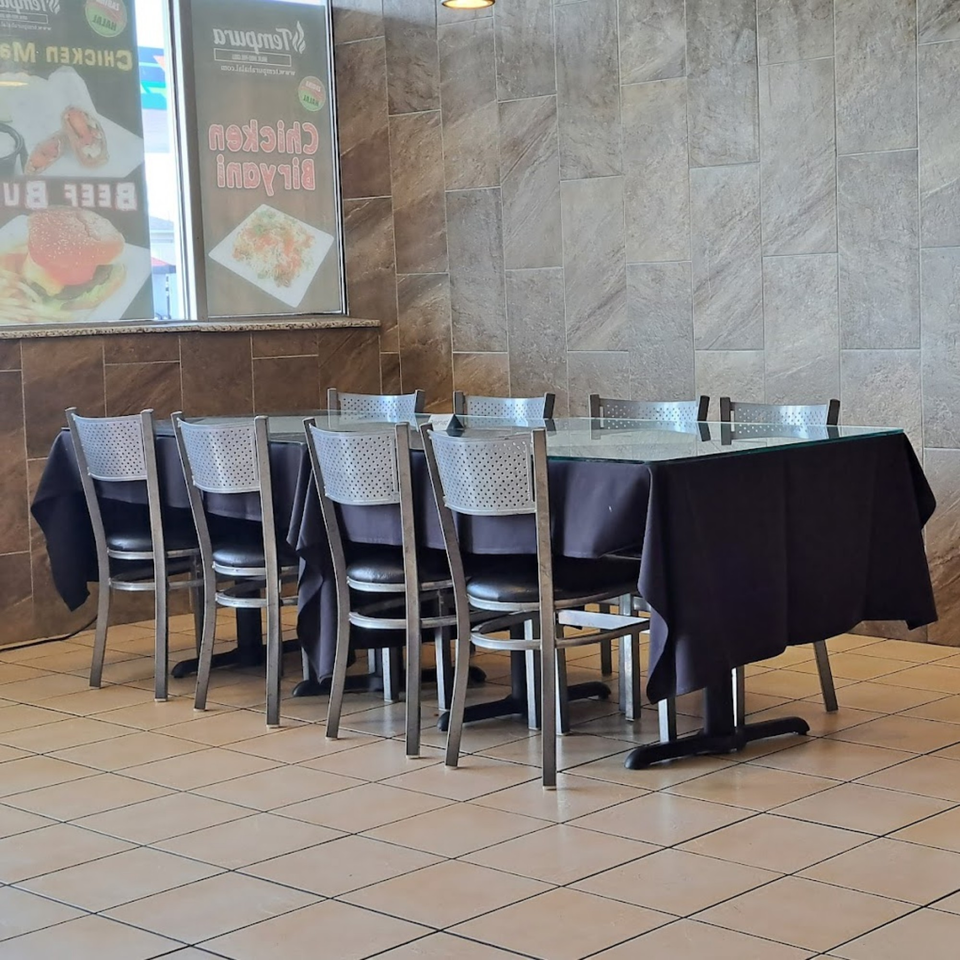 Empty dining area with black-draped tables, metal chairs, and menu posters for Tempura Halal Indo-Pak Grill.