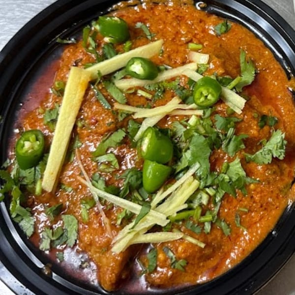 Pakistani chicken karahi, a rich orange curry with green chilies, cilantro, and ginger slivers.