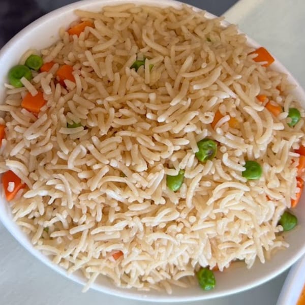A close-up of Pakistani rice pilaf with peas and diced carrots in a white bowl.