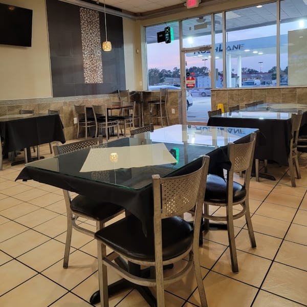 Empty dining room at Tempura Halal Indo-Pak Grill with black-draped tables and tiled floors.
